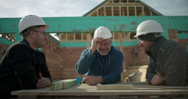 İnşaat işçileri inşaat alanında tartışmalara girdiler, sert şapkalar giydiler, gülümsediler ve etkileşime geçtiler, inşaat sektöründe takım çalışması ve işbirliği yaptılar.