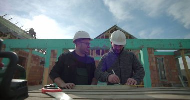 Kesin ölçümler, inşaat alanı, ortak konut projesi, ev iskeleti, çalışma ortamı, takım çalışması, doğruluk ve planlamaya odaklanan araçlar üzerinde çalışan inşaatçılar