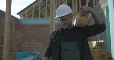 Odaklanmış inşaat işçisi omuzlarında odun destesi taşır, konut inşaatı projesinde takım çalışması, marangozluk görevlerinde kendini adama ve güç