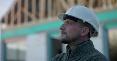 Başlıklı inşaat işçisi, yan profil görüntüsü, inşaat alanındaki odaklanma, açık çerçeve yapısının arka planı, bağlılığı ve vizyonu temsil eden bir yapı işçisi.