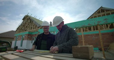 Ahşap tahtaları, takım çalışmasını ve işbirliğini, kalın şapkaları, aletleri, inşaat çalışmalarını ölçmek ve işaretlemek üzere yeni bir ev projesinde birlikte çalışan inşaatçıların yakın plan fotoğrafları.