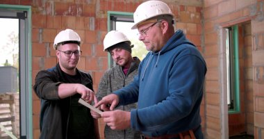 İnşaatçılar, bina planlarını birlikte gözden geçiriyorlar. İnşaat planlama, miğferli üç adam tamamlanmamış yapı projesini tartışıyorlar.