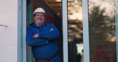 Kapıda duran inşaat işçisi, kollar çapraz, güvenlik teçhizatı giyiyor, inşaat sürecini denetliyor, kendine güvenen duruş, inşaat yönetimi ve denetim