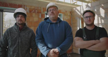 İnşaat ortamında takım çalışması, birlik ve profesyonelliği temsil eden üç inşaat işçisi kısmen inşa edilmiş bir yapıda birlikte duruyorlar.