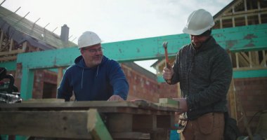 İnşaat alanında ahşap işçiliği üzerine çalışan iki inşaat işçisi, inşaat halindeki konut yapısındaki hassas marangozluğa ve takım çalışmasına odaklanmış durumda.