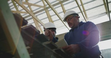 Yapısal çerçeve ve yapı planlarını gözden geçiren inşaat işçileri, yenileme projesinde takım çalışması, ayrıntıları tartışan, sahada güvenlik kaskı takan