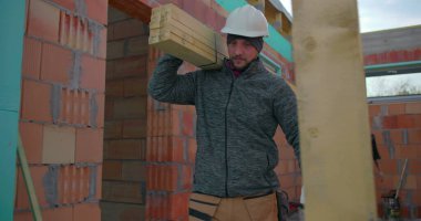 Omuzlarında ahşap kalaslar taşıyan iki inşaat işçisi, konut inşaatında takım çalışması, odaklanmış ifadeler, tuğla duvarlar ve iskelet yapısı