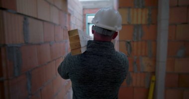 İnşaat işçisi omuzunda ahşap kiriş taşıyor. İnşaat, işçilik ve inşaat sektörünün bitmemiş binasının dar koridorlarında geziniyor.