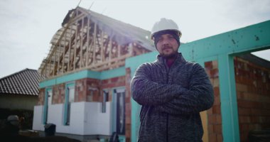 İnşaat alanında kollarını kavuşturarak poz veren erkek inşaat işçisi inşaat sektöründe kendine güveni tam, işçilikte gücü ve gururu var ve çok çalışıyor.