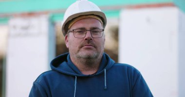 İnşaat işçisi, inşaat alanında ciddi bir ifadeyle ileriye bakıyor. Yüze odaklanıyor, inşaat projesi devam ediyor, açık havada çalışıyor.