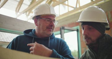 İnşaat alanındaki planları inceleyen inşaat işçilerinin yakın çekimleri, proje planlama ve işbirliği, güvenlik kaskları ve takım çalışması üzerine odaklandı