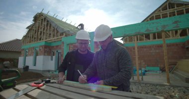 Ahşabı hizalayan ve ölçen iki müteahhit, inşaat alanında takım çalışması, yeni ev iskeleti projesi, konut yapısında işbirliği, sert şapkalar takmak.