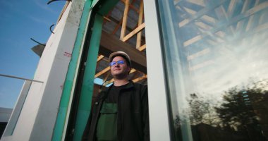 İnşaat işçisi inşaat alanının tamamlanmamış yapı çerçevesi üzerinden gözlüyor. Mavi gökyüzü altındaki bir inşaat projesinde ilerlemeyi değerlendiren baret ve gözlüklü profesyonel.