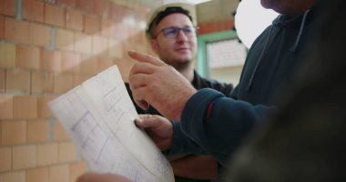 İnşaat planlarını, miğferleri, takım çalışmasını ve işbirliğini tartışan inşaat işçilerinin ayrıntılı görüşü, plan üzerinde yoğunlaşmak, inşaat alanı