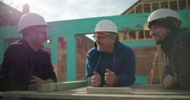 İnşaat işçileri inşaat alanında tartışmalara girdiler, sert şapkalar giydiler, gülümsediler ve etkileşime geçtiler, inşaat sektöründe takım çalışması ve işbirliği yaptılar.