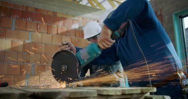 İnşaat alanında metal kesen işçiler, öğütme sırasında uçuşan kıvılcımlar, odaklanmış işçilik, inşaat endüstrisinde takım çalışması, yakın çekim.