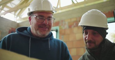 İnşaat alanındaki planları inceleyen inşaat işçilerinin yakın çekimleri, proje planlama ve işbirliği, güvenlik kaskları ve takım çalışması üzerine odaklandı