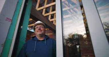 Dışarıya bakan, cam ve ahşap yapısı çerçeveli inşaat işçisi, aktif inşaat alanında sakin tavır.