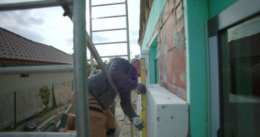 İnşaat sırasında dış duvar yalıtımının ölçülmesi ve seviyelendirilmesi, ev inşaatının enerji tasarrufu için hassas hizalanmasını sağlayan sert şapkalı odaklı müteahhit