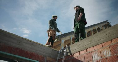 Çatı katındaki inşaat projesini inceleyen inşaat işçileri, ekip çalışması ve haberleşme vurgulandı, konut yapısında güvenlik miğferleri, açık alan inşaatı