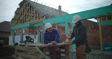 İnşaat işçisi inşaat sahasında meslektaşlarıyla birlikte konut yapı iskeleti projesinde gözlem, takım çalışması ve hassas marangozluk yapıyor.