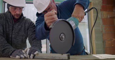 Açı öğütücüyle metali kesen iki inşaat işçisi, yoğun kıvılcımlar, odaklanmış takım çalışması, güvenlik kaskları ve yenileme alanındaki gözlükler.