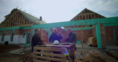 İnşaat alanında pizzayla öğle yemeği arası veren üç müteahhit, gelişigüzel toplanma, takım çalışması ve bağlanma, inşaat halindeki konut projesi.