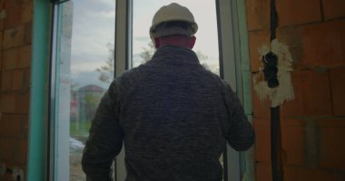 Kask takan inşaat işçisi, konut alanındaki pencere kurulumunu denetleyerek, kalite güvencesi için hassasiyet ve hizalamaya odaklanıyor