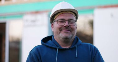 İnşaat işçisi inşaat alanında gülümsüyor, neşeli ifadeye yakın çekim, inşaat projesi, açık hava çalışma ortamı, gündüz çalışma ortamı.