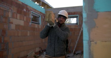 İnşaat alanında uzun ahşap kirişler taşıyan marangozlar, ev yapımı projesinde takım çalışması, kalın şapkalı ve eldivenli iki işçi, konut inşaatı, inşaat malzemeleri.