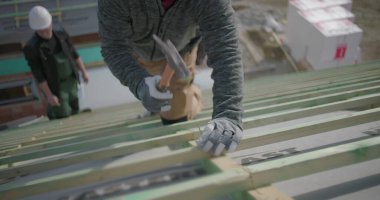 İşçi çatıdaki çivileri güvence altına almak için çekiç kullanıyor, eldiven ve kask takıyor, inşaat alanındaki el ve aletlere yakından bakıyor, proje çalışmalarının bir parçası.