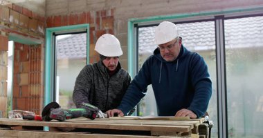 Sert şapkalı iki inşaat işçisi geçici ahşap bir masanın planlarını inceliyor, takım çalışması, planlama, bina inşaatı, işbirliği.