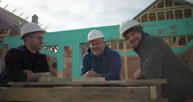 İnşaat işçileri inşaat alanında keyifli bir anı paylaşıyorlar, başlık takıyorlar, sohbet ediyorlar ve işten ayrılırken birbirlerinin arkadaşlığından keyif alıyorlar.