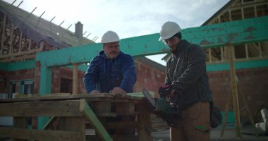 İnşaat işçisi inşaat alanında meslektaşlarıyla birlikte testere kullanıyor, konut inşaatında takım çalışması yapıyor, yapısal çerçeve için odun kesiyor.