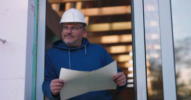 İnşaat planları, güvenlik kaskı ve gözlükleri inceleyen, proje detaylarını ciddi bir ifadeyle değerlendiren, kendinden emin ve profesyonel duruş sergileyen bir işçi.