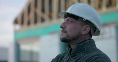 Başlıklı inşaat işçisi, yan profil görüntüsü, inşaat alanındaki odaklanma, açık çerçeve yapısının arka planı, bağlılığı ve vizyonu temsil eden bir yapı işçisi.