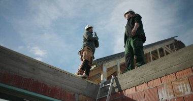 Çatı katındaki inşaat projesini inceleyen inşaat işçileri, ekip çalışması ve haberleşme vurgulandı, konut yapısında güvenlik miğferleri, açık alan inşaatı