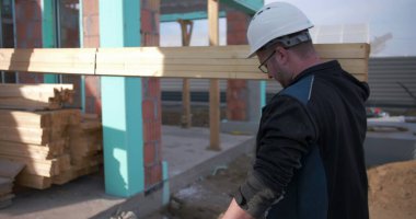 İnşaat işçisi omuzunda uzun ahşap kalaslar taşıyor, inşaat alanı boyunca malzeme taşıyor marangozlukta takım çalışması ve dayanıklılık için.