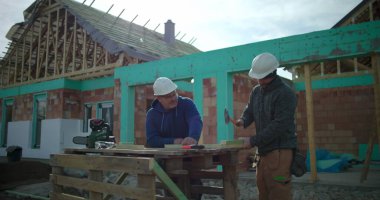 İnşaat işçisi inşaat sahasında meslektaşlarıyla birlikte konut yapı iskeleti projesinde gözlem, takım çalışması ve hassas marangozluk yapıyor.