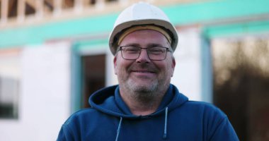 İnşaat işçisi inşaat alanında gülümsüyor, neşeli ifadeye yakın çekim, inşaat projesi, açık hava çalışma ortamı, gündüz çalışma ortamı.