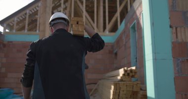 İnşaat alanında ahşap kalaslar taşıyan işçiler, konut inşaatında işbirliği, sert şapkalı adamlar, tuğla duvarlar ve arka planda ahşap kirişler.