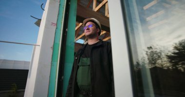 İnşaat işçisi inşaat alanının tamamlanmamış yapı çerçevesi üzerinden gözlüyor. Mavi gökyüzü altındaki bir inşaat projesinde ilerlemeyi değerlendiren baret ve gözlüklü profesyonel.