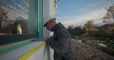 İnşaat duvarı boyunca mezurayı dikkatlice hizalayan işçiler, inşaat doğruluğu, odaklanmış ifade, tesis kurulumu ve kurulum süreci için ölçümler alıyor