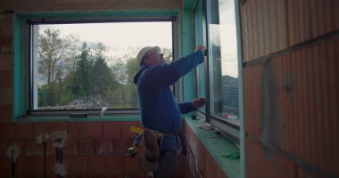 Konut inşaatı projesinde pencere kurulumunu doğrulayan inşaat işçisi, hizalama ve sığdırmaya odaklandı