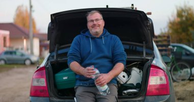 İnşaat alanında mola veren işçiler, araba bagajında oturup su şişesi tutanlar, açık hava yenileme projesi sırasında gevşeme ve esnekliği vurgulayanlar,