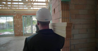 İnşaat işçileri miğferleriyle inşaat halindeki ahşap kalasları, taşınan malzemeleri, inşaat projesindeki takım çalışmasını ve organizasyonu taşıyorlar.