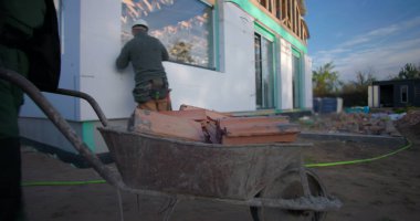 İnşaat alanında ahşap malzemelerle dolu bir el arabasını iten adam inşaat, açık hava inşaatı, takım çalışması ve el işçiliğine odaklanıyor.