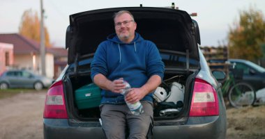 İnşaat alanında mola veren işçiler, araba bagajında oturup su şişesi tutanlar, açık hava yenileme projesi sırasında gevşeme ve esnekliği vurgulayanlar,