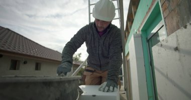 Kovadan havan topu çıkarmak, dış duvardaki yalıtım işleri için güvenlik donanımlı inşaat işçisi, arka planda kask, eldiven ve merdiven ile yakın plan.