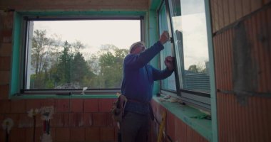 Elle çalışan kişi, konut inşaatı alanındaki pencere montajını, çerçeve hizalamasını ve güvenli kurulum için kalite standartlarını denetliyor